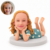 custom bobblehead figure girl lying on her tummy with both hands cupping her cheeks and both knees bent up