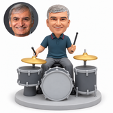 custom bobblehead figure male drummer seated at a three-drum kit with two cymbals and one drumstick raised