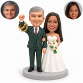 custom bobblehead figures wedding couple with the groom raising one fist beside decorative ring loops and the bride linking his arm while holding a bouquet