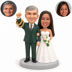 custom bobblehead figures wedding couple with the groom raising one fist beside decorative ring loops and the bride linking his arm while holding a bouquet