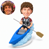 custom bobblehead figure male kayaker holding a single-bladed paddle across his lap in a blue kayak on a wave base