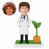 custom bobblehead figure male doctor with both hands in his coat pockets beside a sculpted potted plant