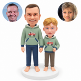 custom bobblehead figures father and son holding hands while standing barefoot with the father's outer arm down and the boy's outer hand bent at his waist