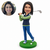 Custom female golfer bobblehead finishing a golf swing with both hands on a club over the shoulder and a golf ball on the base