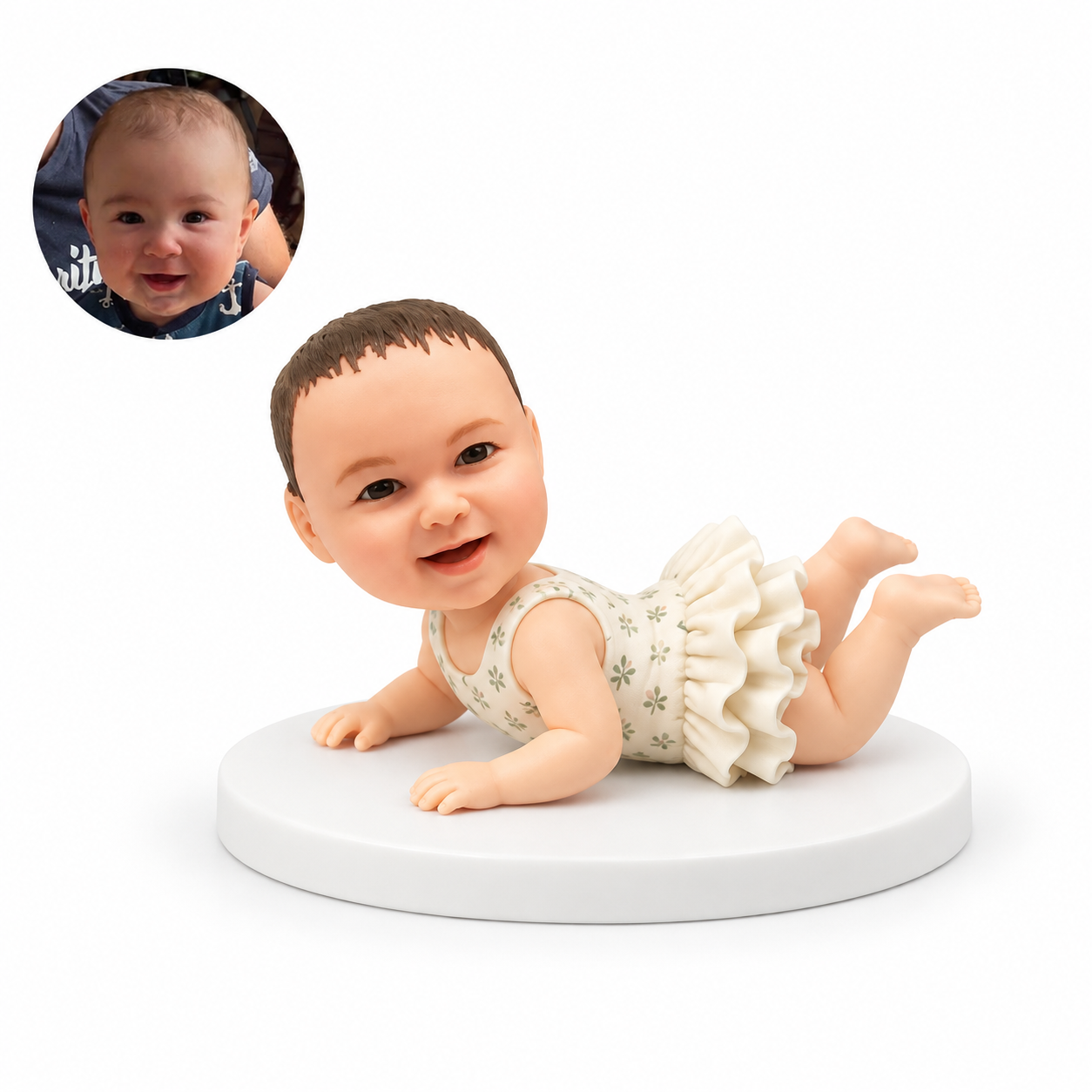 Custom soft-clay baby bobblehead lying on the tummy with both palms on a white base and both bare feet raised, beside a matching real baby portrait