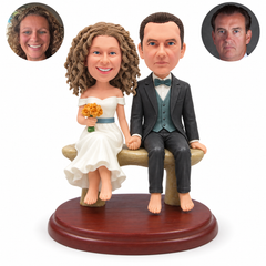 Custom clay barefoot wedding couple seated hand in hand on a backless bench, bride holding a bouquet, with matching real photo portraits.