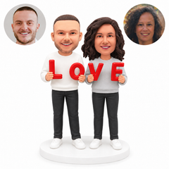 Custom couple bobblehead with man on left holding L and O and woman on right holding V and E, on a white base