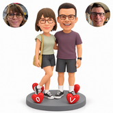 Custom clay couple, woman left with crossed leg and shoulder bag, man right, four fixed heart ornaments on an oval base