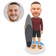 custom bobblehead figure surfer in a long-sleeve shirt and flip-flops holding a surfboard on a beach base