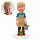 custom bobblehead figure female gardener carrying a watering can beside potted flowers