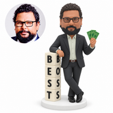 custom bobblehead figure businessman with crossed ankles resting one arm on a best boss block tower while holding banknotes