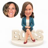 custom bobblehead figure woman in a skirt seated on BOSS letters with crossed legs and hands folded on her lap MGA-AC1202