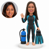 custom bobblehead figure female scuba diver giving an OK gesture and holding fins beside an air tank MGA-AC1311