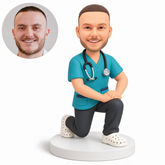 custom bobblehead figure male doctor in scrubs kneeling on one knee with both hands resting on his raised knee - original own-site polymer clay head and matched photo