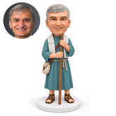 custom bobblehead figure man in an ancient robe and shoulder wrap gripping a staff with both hands beside a hip satchel