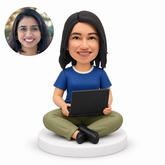 custom bobblehead figure woman sitting cross-legged directly on a round base holding an open laptop on her lap