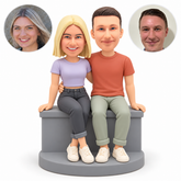 custom bobbleheads figures couple sitting on a low wall with their inner arms around each others waist