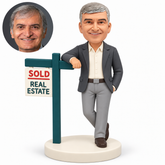 custom bobblehead figure business man leaning one forearm on a real estate sign post