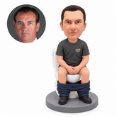 Custom clay bobblehead man seated on a toilet with hands clasped and trousers at ankles
