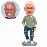 Clay man in a sage top and indigo jeans, right hand in trouser pocket, left empty arm down, right knee bent with heel raised, on a gray round base with matching real portrait.