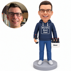 Clay dad in a navy World’s Best Dad hoodie, both arms lowered with one bottle low at his right thigh and a white bottle carrier at his left, gray base and matching real portrait.
