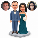 Clay wedding couple: groom in a slate blue suit with both arms lowered, bride in a teal gown holding a side rose bouquet, gray heart base and paired real portraits.