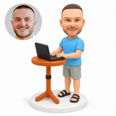 custom bobblehead figure man in a T-shirt and shorts using a laptop on a pedestal table