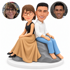 custom bobblehead figures couple seated back to back on a rock with the woman in a long skirt and the man in a shirt and jeans