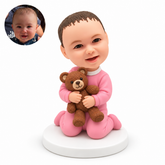 custom bobblehead figure baby kneeling in a footed onesie while hugging a teddy bear