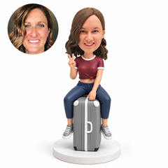 custom bobblehead figure woman seated on an upright suitcase making a peace sign