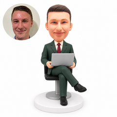 custom bobblehead figure businessman seated with his right leg crossed holding an open laptop on his lap with both hands