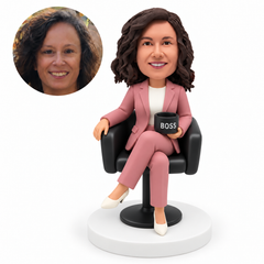 custom bobblehead figure woman seated with crossed legs in an armchair holding a cup with her other hand on the armrest