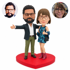 Polymer-clay couple on a red heart base: man with an outstretched arm, woman giving a thumbs up, and matching portrait photos