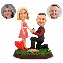 Custom clay kneeling proposal couple: woman in dusty rose dress, man in burgundy shirt and charcoal vest with ring box, red heart and pink roses on grassy base, matching portrait photos