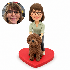 Custom bobblehead figure of a woman in a sage blouse resting both hands on a large seated curly brown dog, on a red heart base, with matching portrait inset.