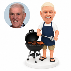 custom bobblehead figure man in an apron holding a spatula beside a kettle grill