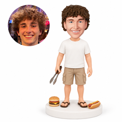 custom bobblehead figure man holding barbecue tongs beside a burger and hot dog