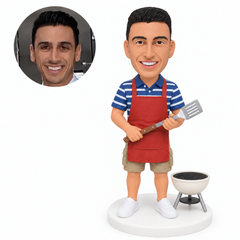 custom bobblehead figure man holding a spatula beside a small kettle barbecue