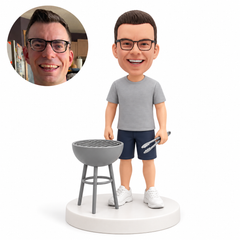 custom bobblehead figure man holding tongs beside a simple kettle grill