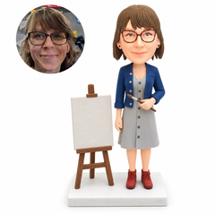 custom bobblehead figure female art teacher in a dress holding a paintbrush beside an easel