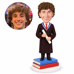 custom bobblehead figure male graduate in a maroon gown holding a diploma on stacked books