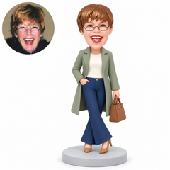 custom bobblehead figure woman in a long jacket with crossed ankles carrying a handbag and a hand in a trouser pocket MGA-AC1275