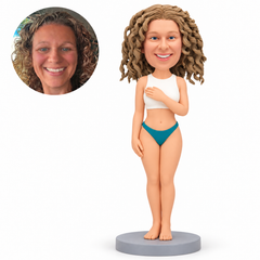 Clay adult woman in an ivory athletic top and teal swim briefs, left open hand across her chest, right hand down and close bare feet on a gray base, with matching real portrait.