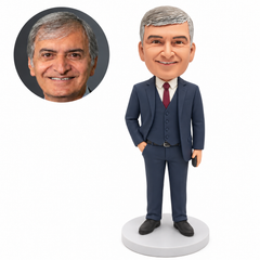 Custom polymer-clay man in a navy three-piece suit, right hand in his trouser pocket and left hand holding a small dark rectangular accessory low beside his thigh, with matching real portrait