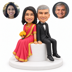 custom bobblehead figures bride in a sari and groom in a formal suit seated back to back on a round stool